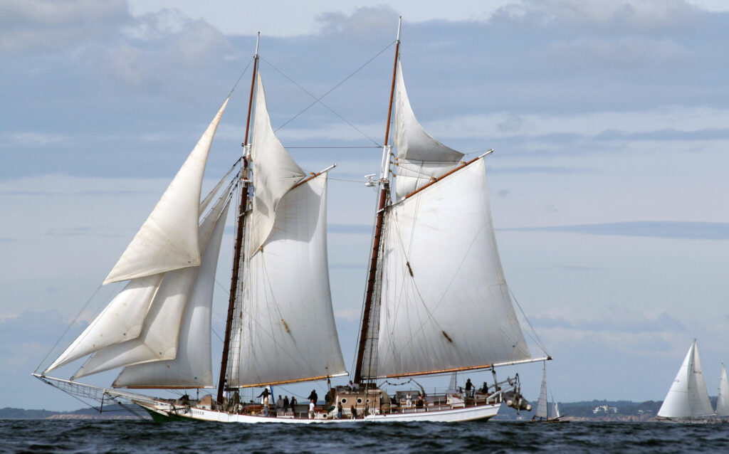 Schooner sails over the ocean waves in the bay near a harbor.